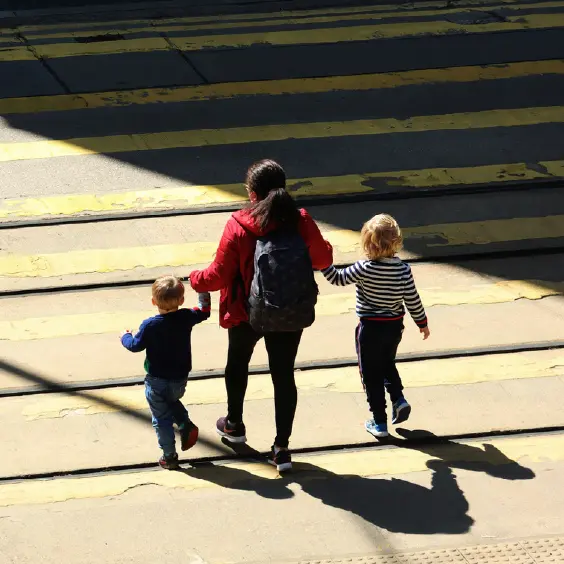A mother crosses the street with two children holding their hands