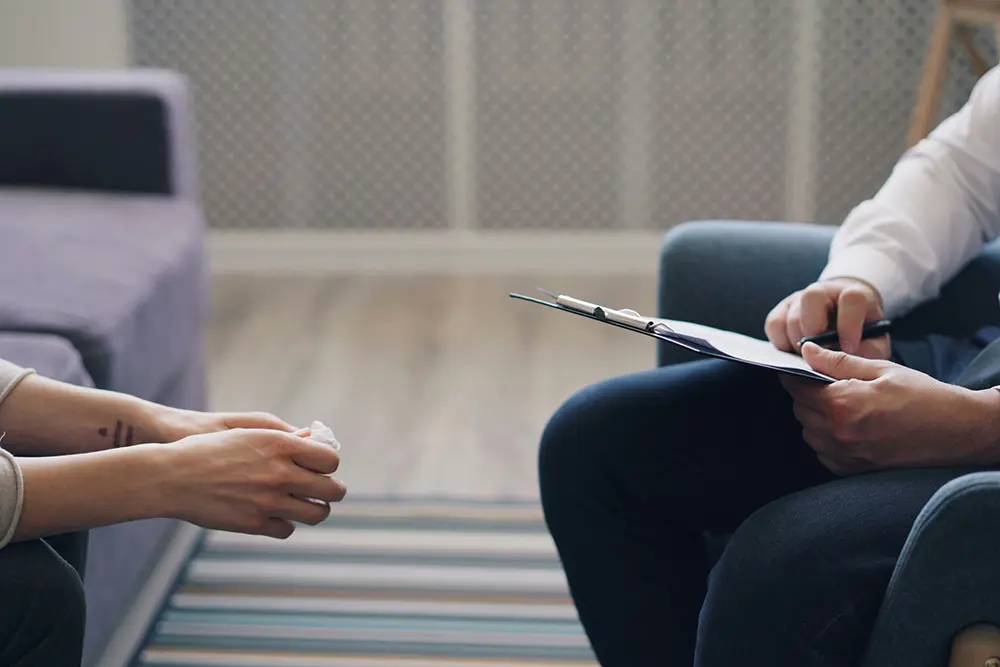 Closeup of a case manager taking notes while talking to a client sitting on a couch