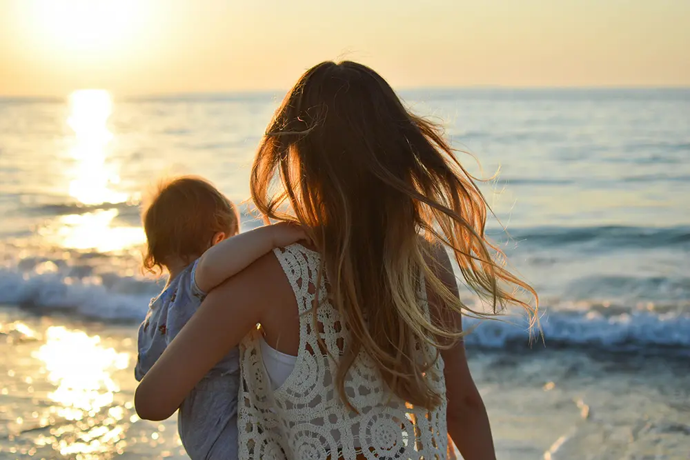 A young mother holds her baby at the ocean at sunset